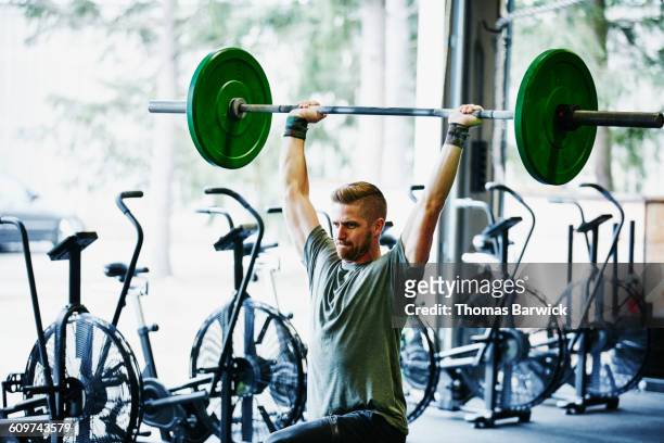 man doing lunges with barbell overhead in gym - mann gewichtheben stock-fotos und bilder