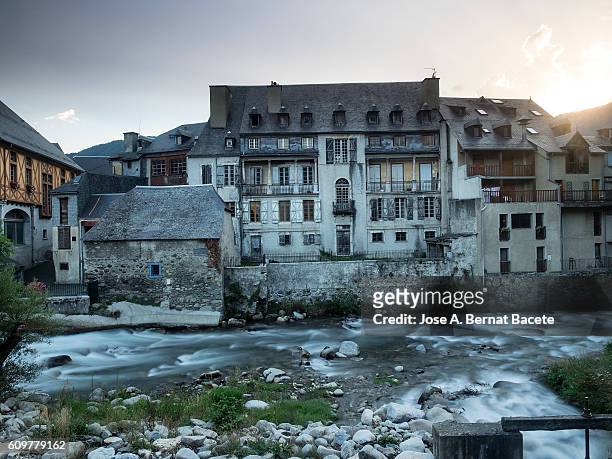 old house facing a river running through the village in france  pyrenees, (arreau) - castle france stock-fotos und bilder