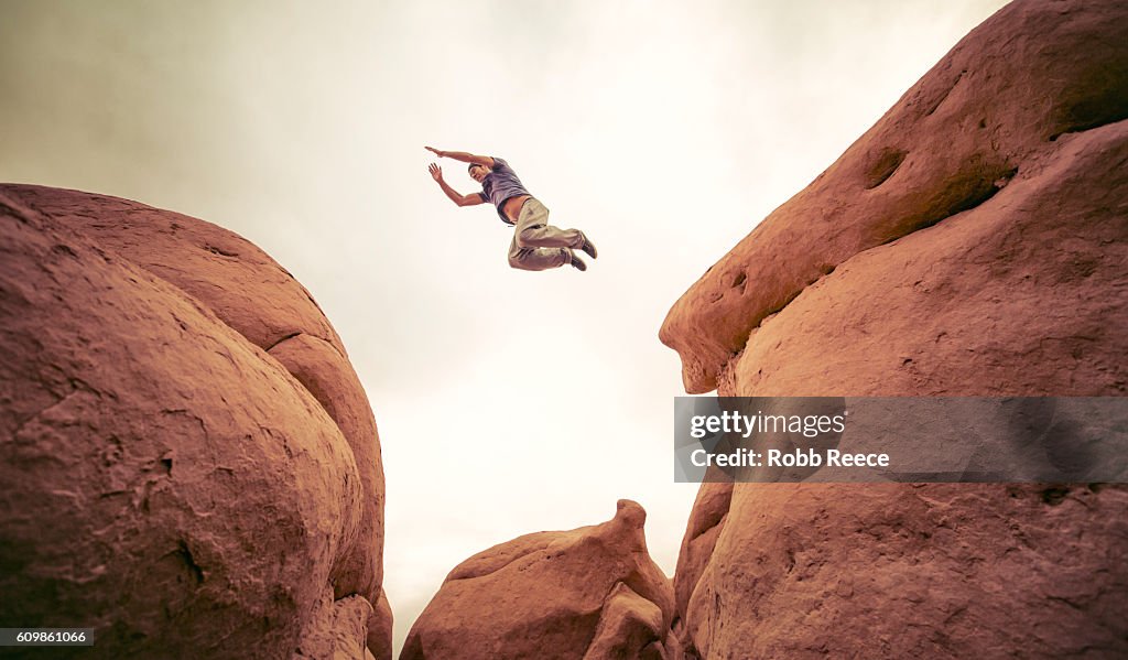 A man performing parkour outdoors on rock formations in the desert