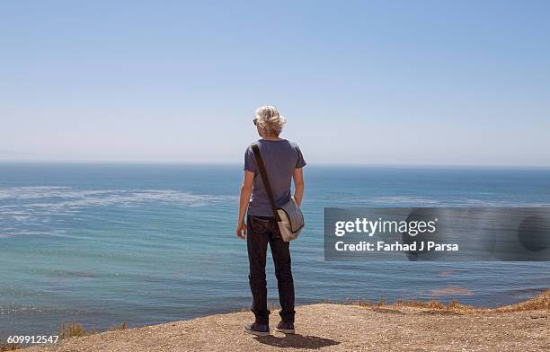 man stands by cliff's edge over the ocean - cliff edge stock-fotos und bilder