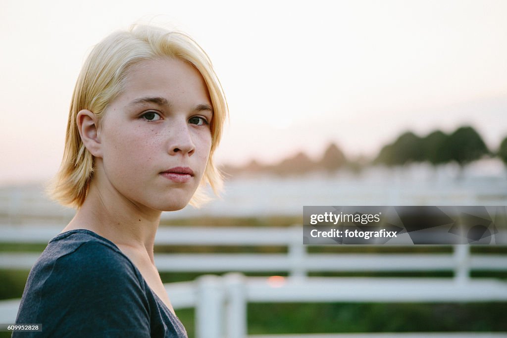 Portrait: cute blonde teenager girl looks seriously at the camera