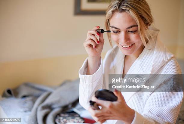 young woman in a bathrobe doing her makeup - woman mascara stock pictures, royalty-free photos & images