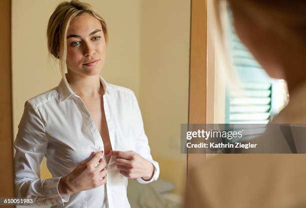 young woman getting dressed in front of mirror - women white shirt stock pictures, royalty-free photos & images