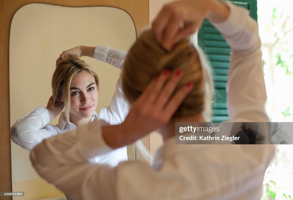 Young woman doing her hair in front of mirror