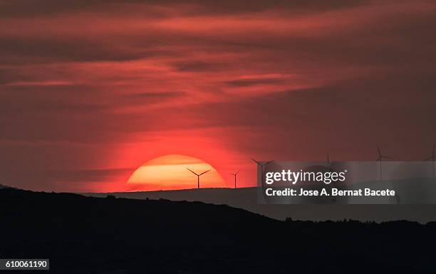 the first plane of a putting sun, hiding between mountains with wind mills - electricity pylon stock pictures, royalty-free photos & images