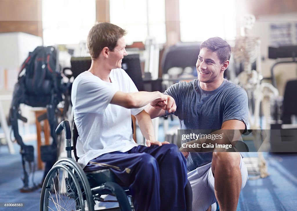 Physical therapist fist bumping man in wheelchair