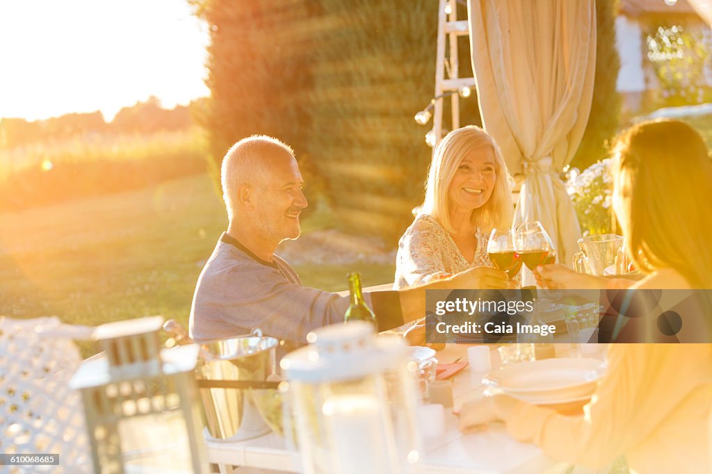 Senior couple an adult daughter toasting wine glasses at sunny patio table