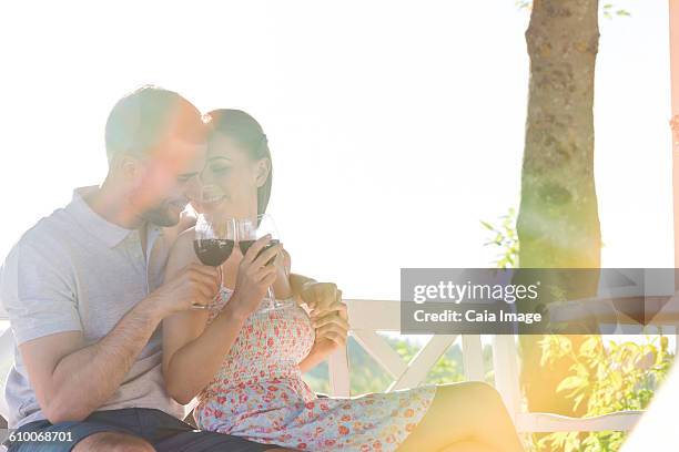 affectionate couple hugging and drinking red wine on sunny bench - young couple red sunny stockfoto's en -beelden