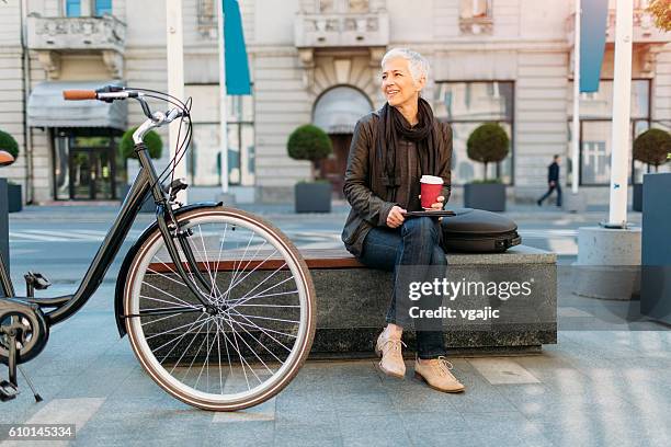 smiling mature woman using digital tablet outdoors. - mature women coffee stock pictures, royalty-free photos & images