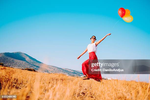 happy woman walking in the field and holding balloons - multi coloured skirt stock pictures, royalty-free photos & images