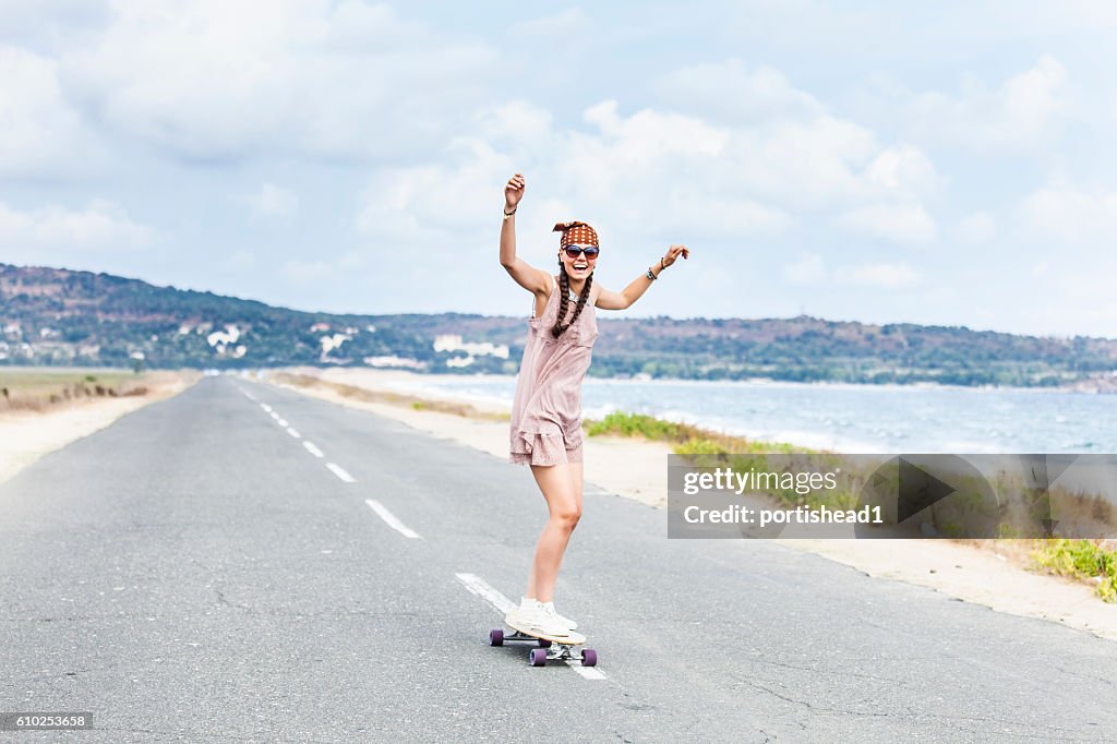 Cheerful young woman skateboarding on road next to the sea