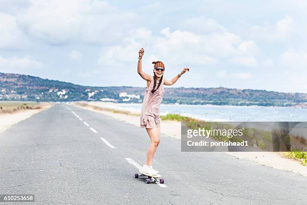 cheerful young woman skateboarding on road next to the sea - surfar com prancha longa imagens e fotografias de stock