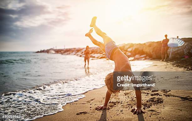 garotinho praticando carrinho de mão na praia - handstand - fotografias e filmes do acervo