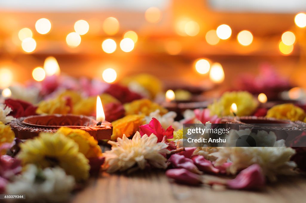 Diya lamps lit during diwali celebration with flowers and sweets in background