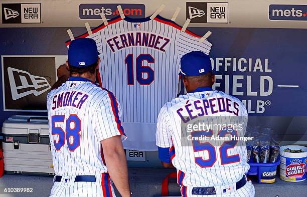 Yoenis Cespedes of the New York Mets and Josh Smoker of the New York Mets hang a jersey for Jose Fernandez of the Miami Marlins in their dugout prior...