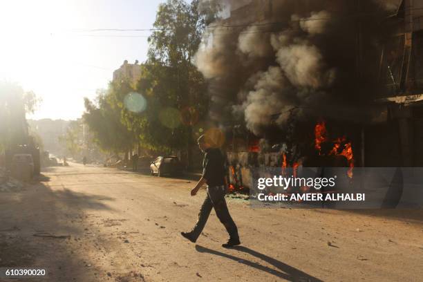 Syrian man walks past a bus set ablaze following a reported air strike in the rebel-held Salaheddin district of Aleppo on September 25, 2016. The UN...