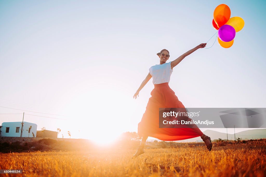 Beautiful young woman running in the field with balloons