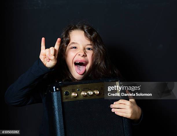 cute smiling boy with long hair with amplifier making rock and roll sign - rock n roll stock-fotos und bilder