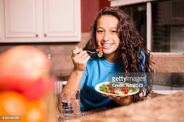teenage girl eating salad for dinner after school. - child eating a fruit stockfoto's en -beelden