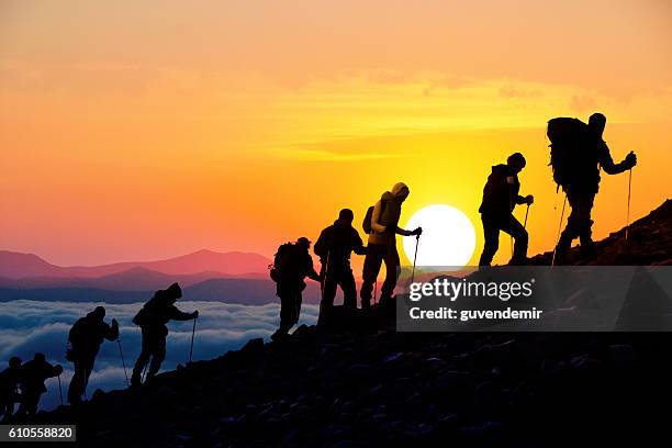 silhouettes of hikers at sunset - team climbing up to mountain top stockfoto's en -beelden