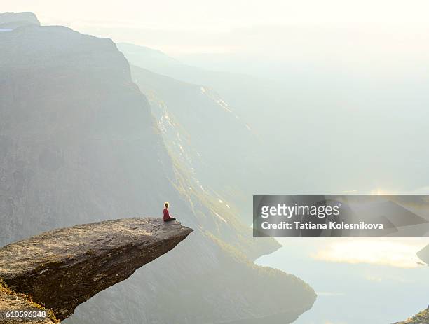woman sitting on the edge of a cliff - imponente fotografías e imágenes de stock