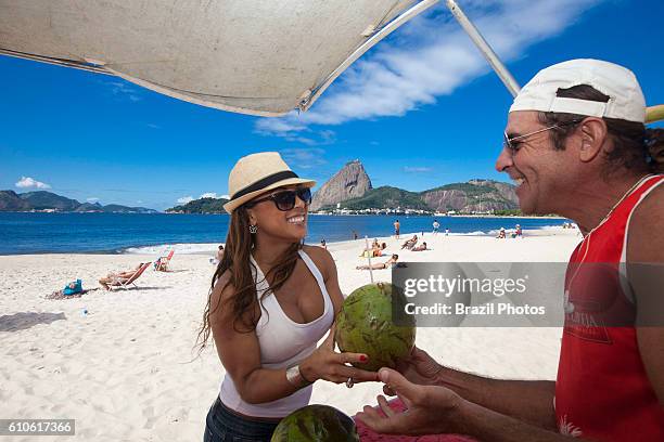 Pretty brunette Brazilian woman drinks coconut water at Flamengo beach, Sugarloaf mountain in background, Rio de Janeiro, Brazil.