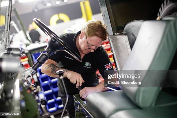 An employee makes adjustments under the driver's seat of a Land Rover Series One automobile at Land Rover's Classic Workshop in Solihull, U.K. On...