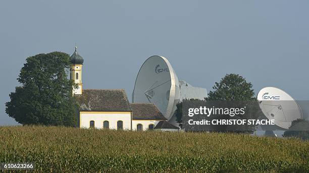 Parabolic antenna's stand behind the Baroque church of Saint John in Raisting near Weilheim, southern Germany, during nice autumn weather with...