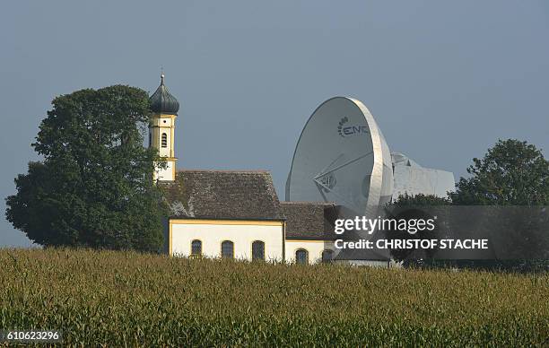 Parabolic antenna stands behind the Baroque church of Saint John in Raisting near Weilheim, southern Germany, during nice autumn weather with...