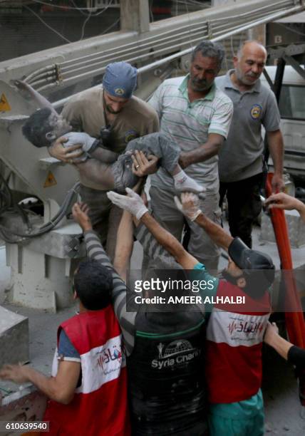 Syrian civil defence volunteers, known as the White Helmets, pass the body of a boy after he was pulled from the rubble following a government forces...