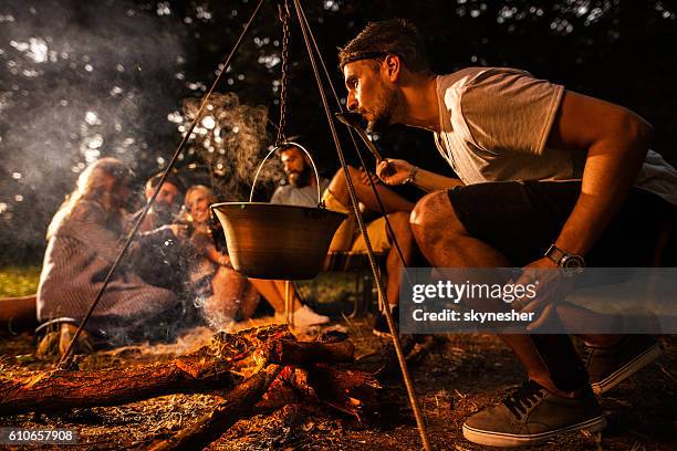 young man preparing food while camping with his friends. - cauldron stock pictures, royalty-free photos & images