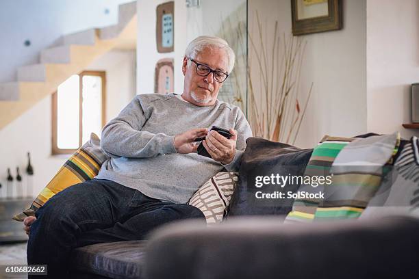 mature man using smartphone - white sofa stock pictures, royalty-free photos & images