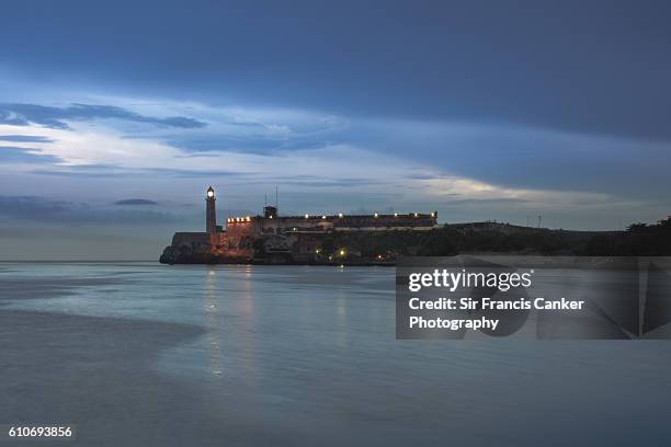 old stone lighthouse and el morro castle illuminated at dusk in havana, cuba - antilles stock-fotos und bilder