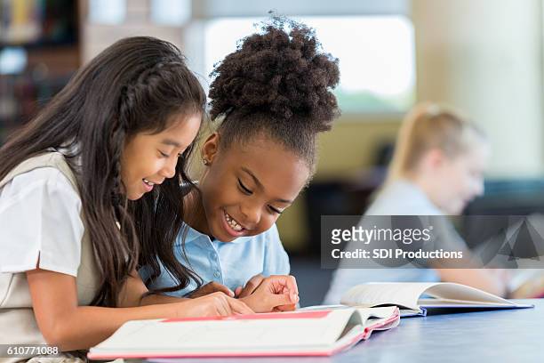 smiling and cheerful schoolgirls reading a book together at school - kids reading imagens e fotografias de stock