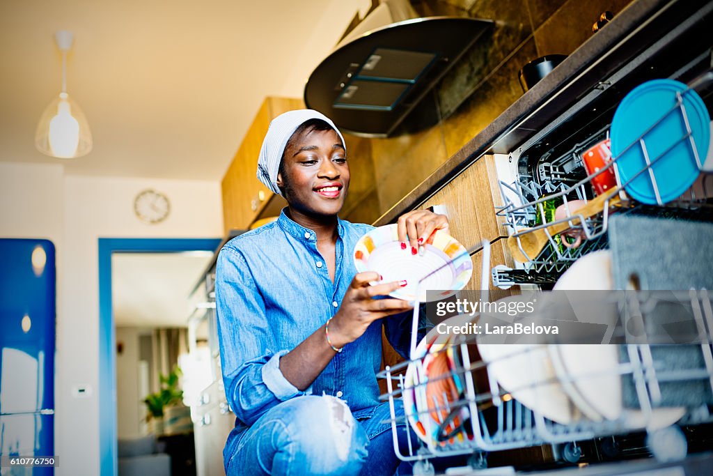 Young African woman using dishwasher in domestic kitchen