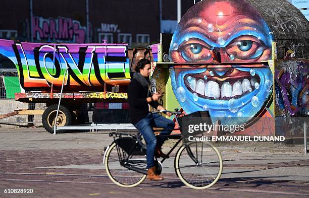 Person rides a bike in front of street artist's works at at the NDSM shipyards, in Amsterdam, on September 27, 2016. / AFP / EMMANUEL DUNAND /...