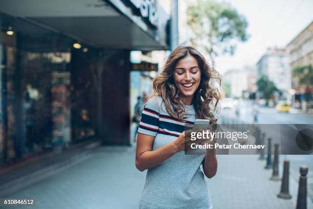 smiling girl texting on the street - fashionable girl stock pictures, royalty-free photos & images