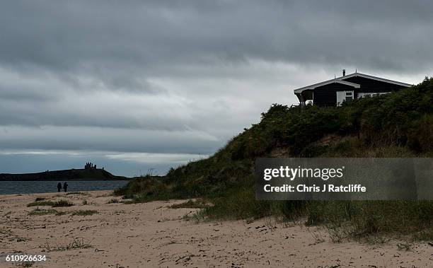 Beach house sits on top of sand dunes in Embleton Bay as dark storm clouds form over Dunstanburgh Castle on the coast of Northumberland on September...