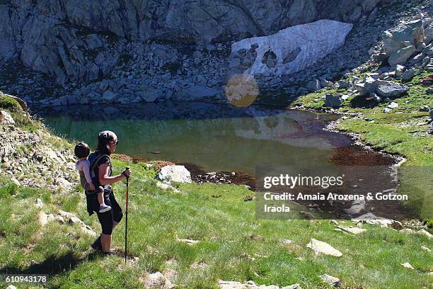 pyrenees, huesca province, spain. mother hiking and carrying her little daughter in backpack near bachimaña glacial lake - provinz huesca stock-fotos und bilder