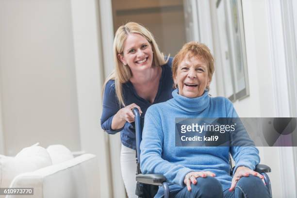 senior woman in wheelchair with caregiver at home - disability care stockfoto's en -beelden