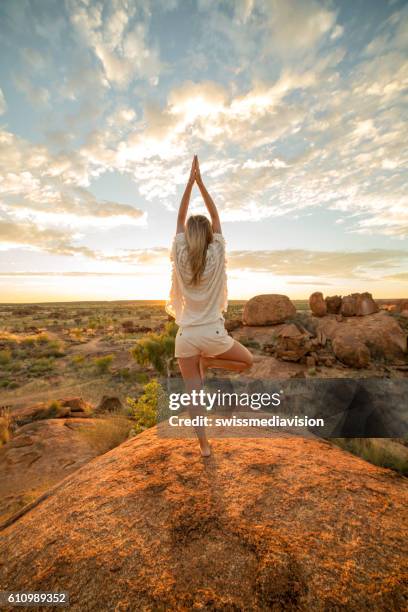 female on boulder exercises yoga at sunrise - yoga retreat stock pictures, royalty-free photos & images