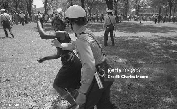 In Kelly Ingram Park, after being knocked down by the water from a firehose, an anti-segregation demonstrator shakes off a police officer who tries...