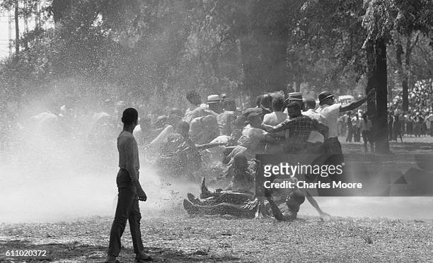 In Kelly Ingram Park, anti-segregation demonstrators are knocked down by the water from a firehose, Birmingham, Alabama, early May, 1963. Police...