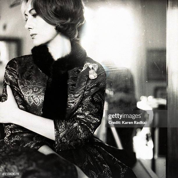 Helene Rochas, wearing white dinner dress by Guy Laroche, seated on chair arm.