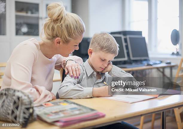 young pupil studying with teacher at school desk - estonia school stock pictures, royalty-free photos & images