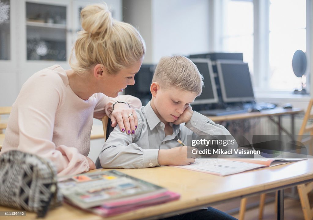 Young pupil studying with teacher at school desk