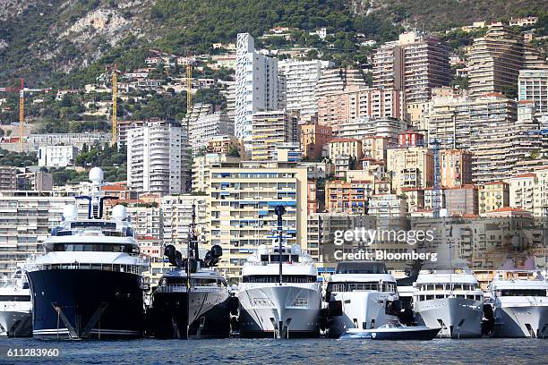 Luxury yachts sit moored in the harbor as hotels and residential property sit along the coastline beyond during the Monaco Yacht Show in Port...