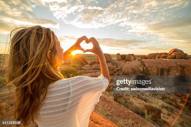 young woman makes heart shape finger frame to spectacular landscape-sunrise - australia women stockfoto's en -beelden