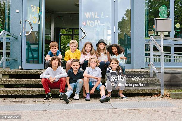 grundschüler sitzen vor dem schulgebäude - elementary school building stock-fotos und bilder