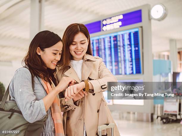 two ladies using smart watch at airport - departure board front on fotografías e imágenes de stock
